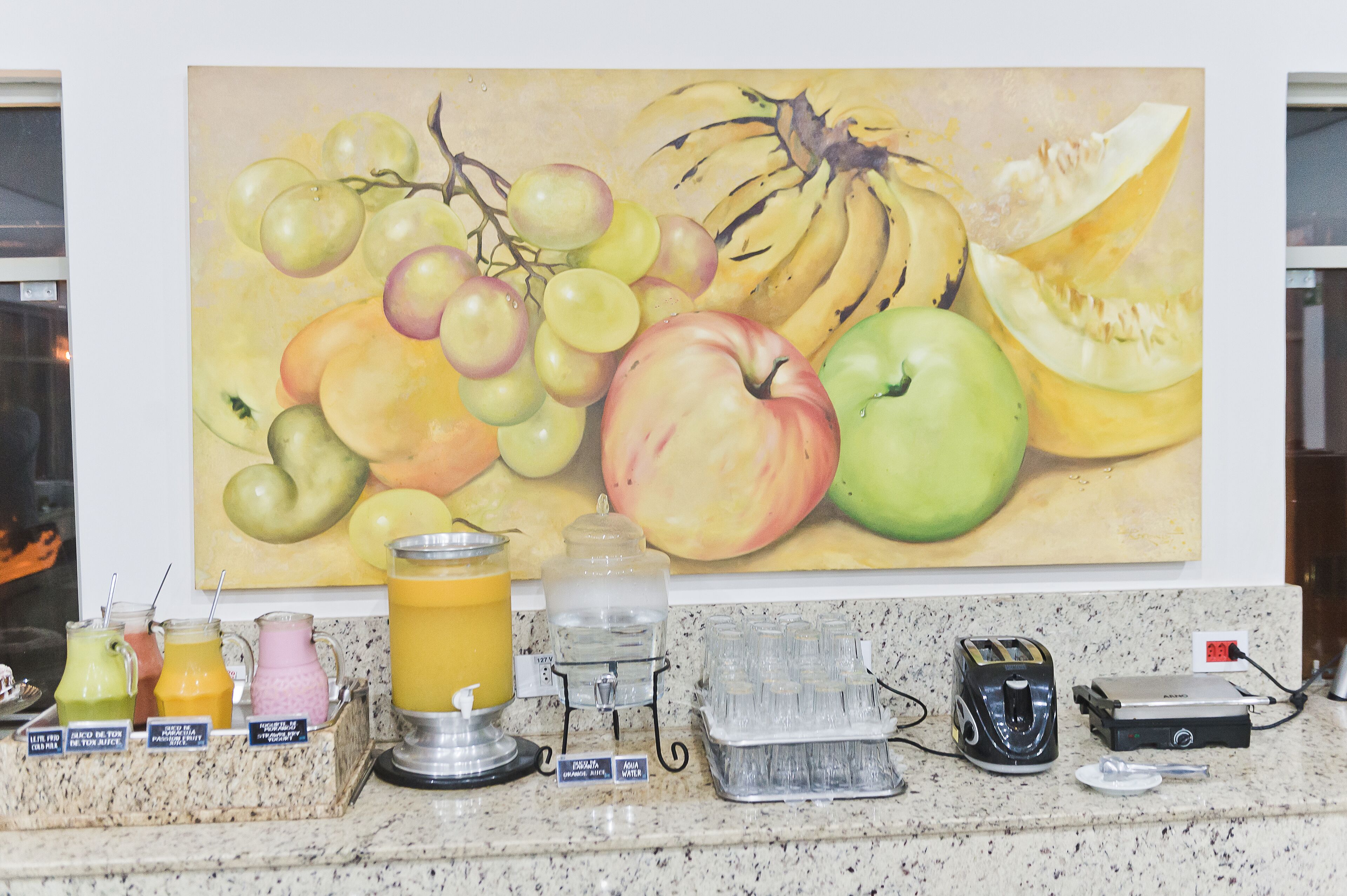 Een aanrecht met een fruit schilderij, een waterdispenser en een broodrooster.