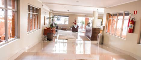 A spacious lobby with a polished floor, large windows, and a fire extinguisher on the wall.