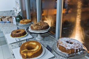 A display of various cakes on a marble countertop with a glass display case in the background. - Hotel Pousada Ourinhos (Ourinhos)
