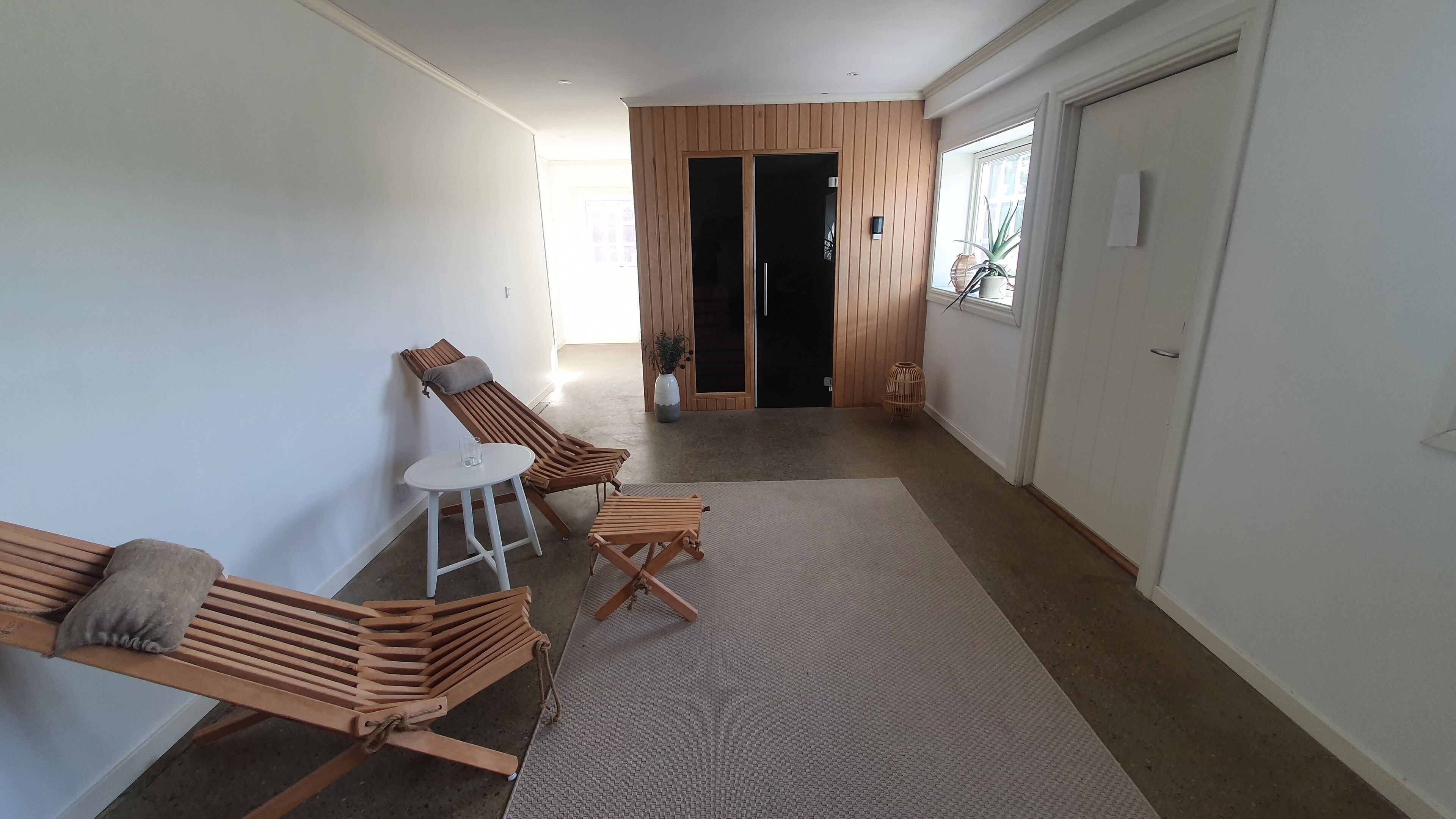 Un pasillo con dos sillones de madera, una mesita blanca y un tapete grande.