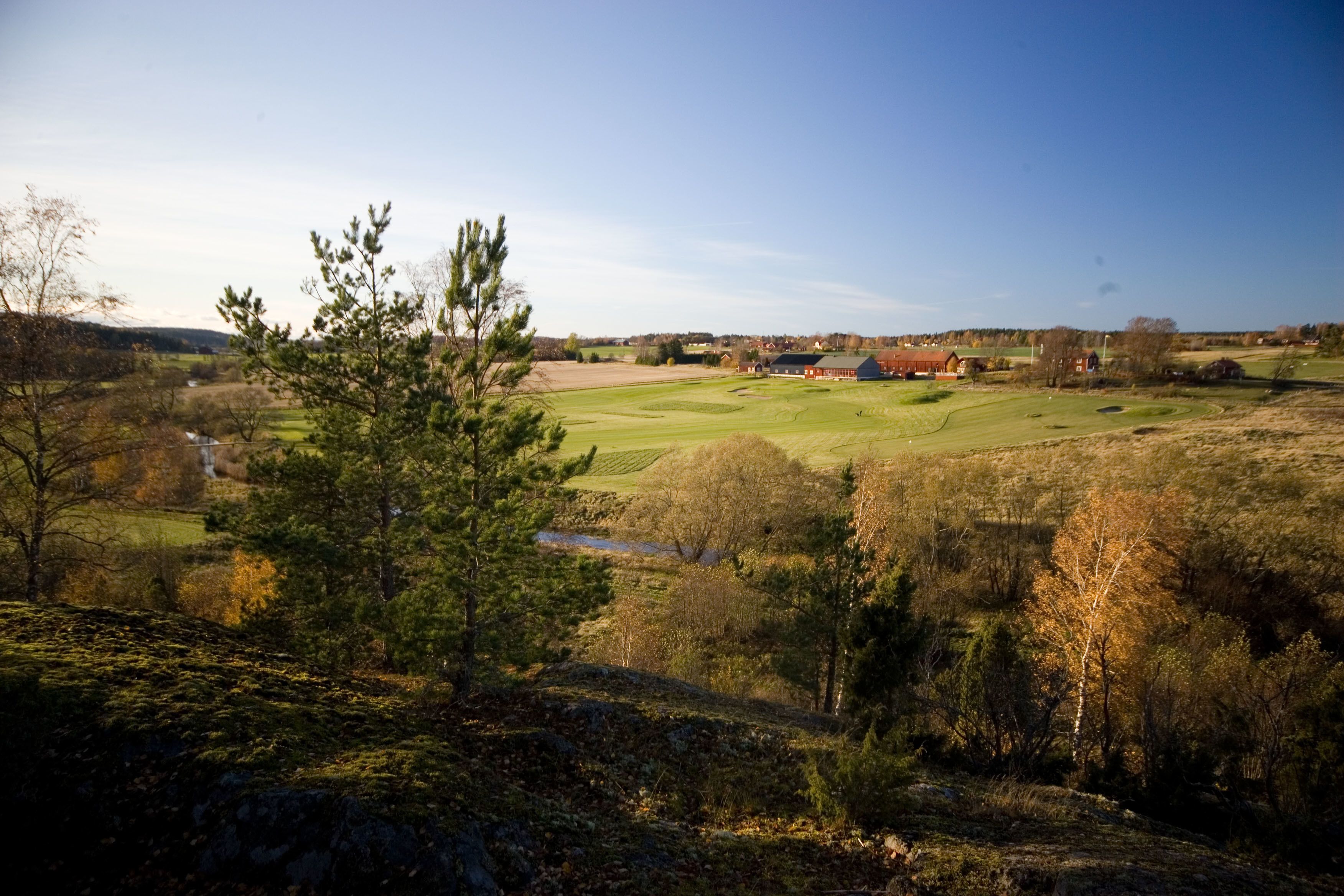 A rural landscape with a golf course, a red barn, and a small house in the distance.