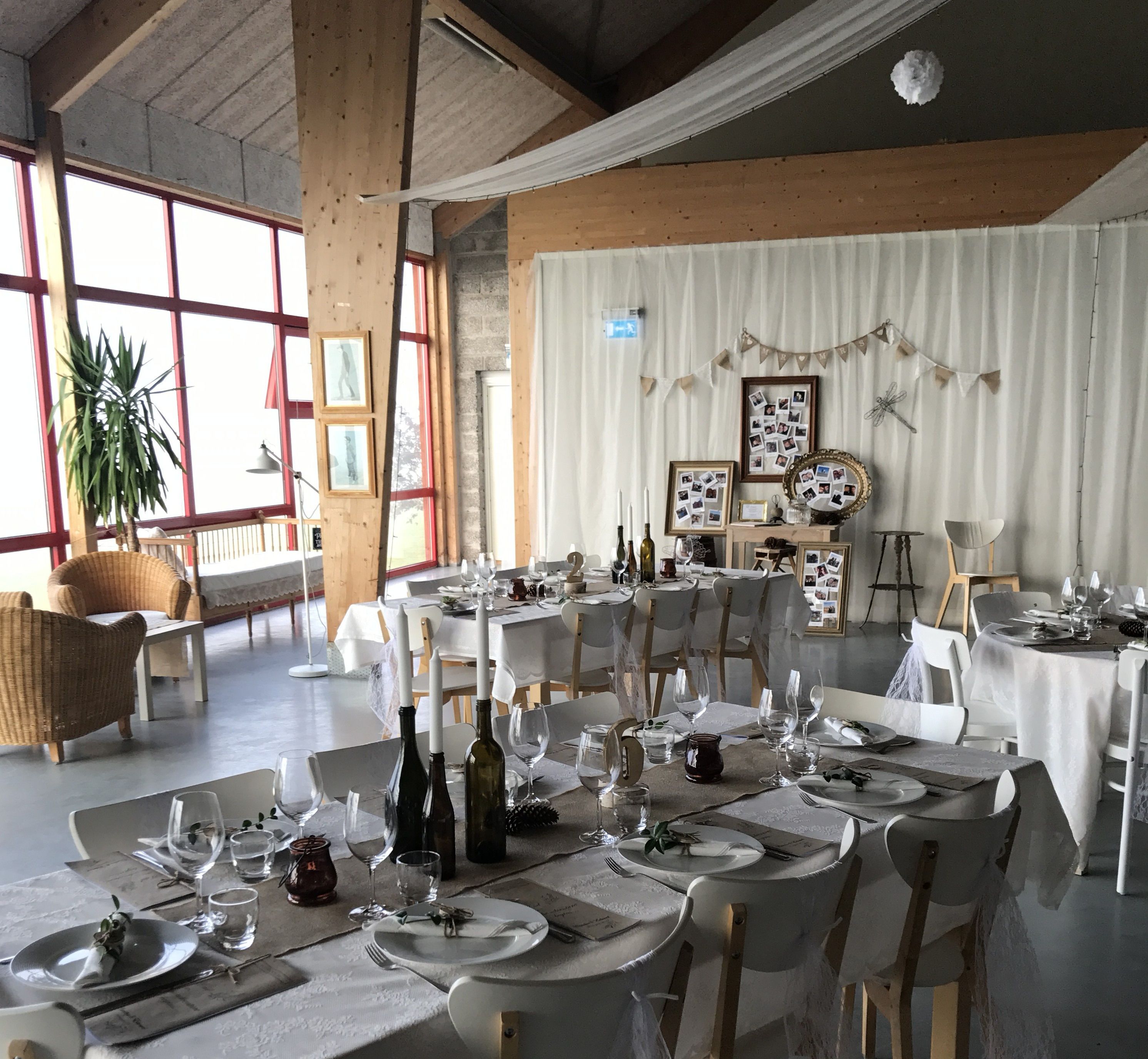 Un comedor amplio con varias mesas dispuestas para una comida, con manteles blancos, copas de vino y botellas.