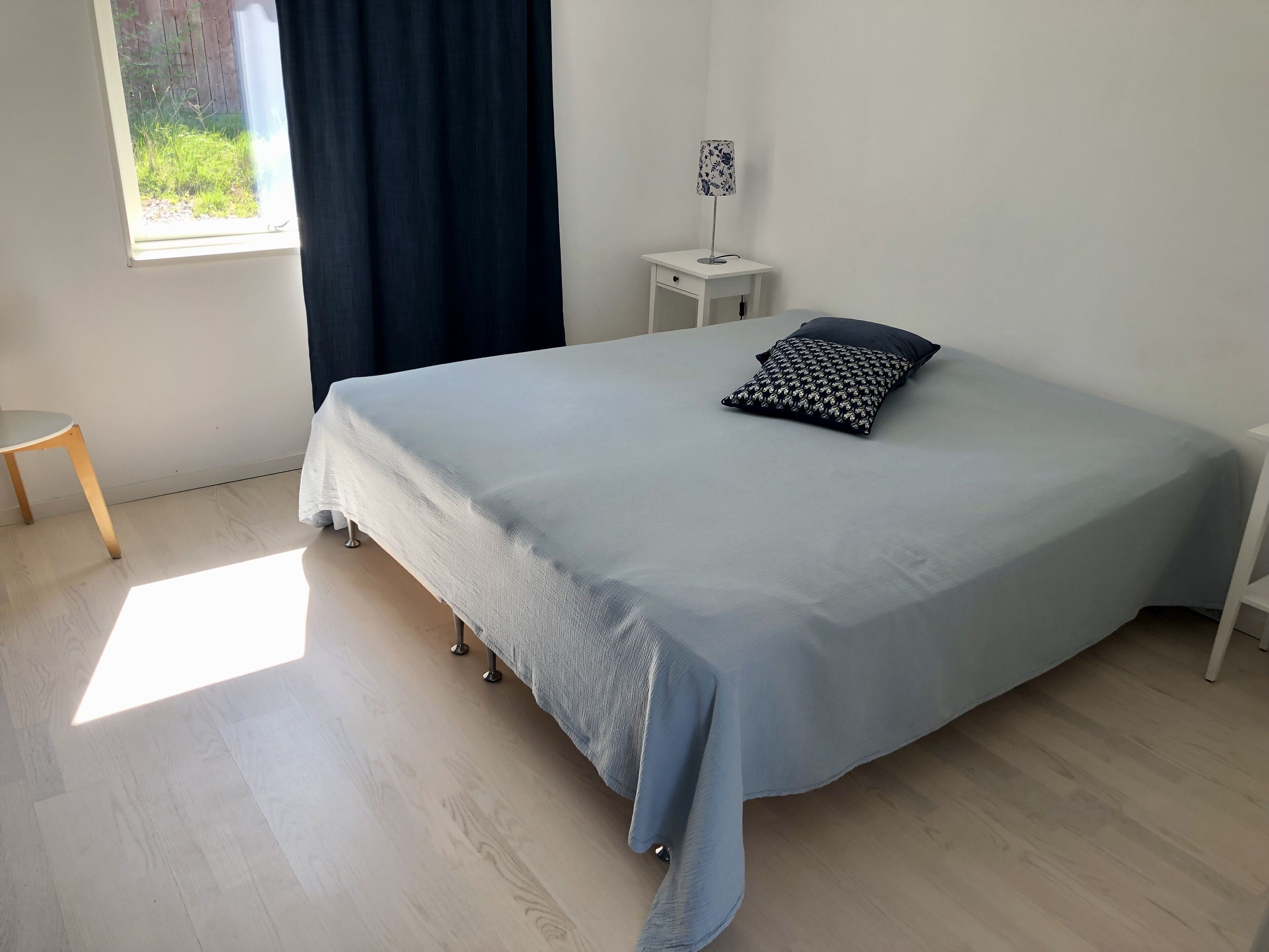 A bedroom with a bed, a bedside table, a lamp, and a window with curtains.