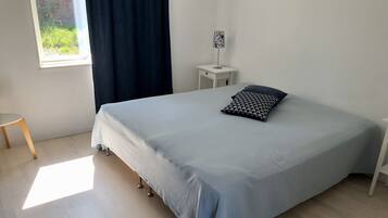 A bedroom with a bed, a bedside table, a lamp, and a window with curtains.
