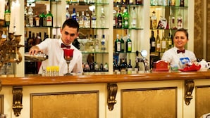 Et barområde med en bartender, der laver drinks. Baren har en trædisk og reoler fyldt med diverse flasker og glas.