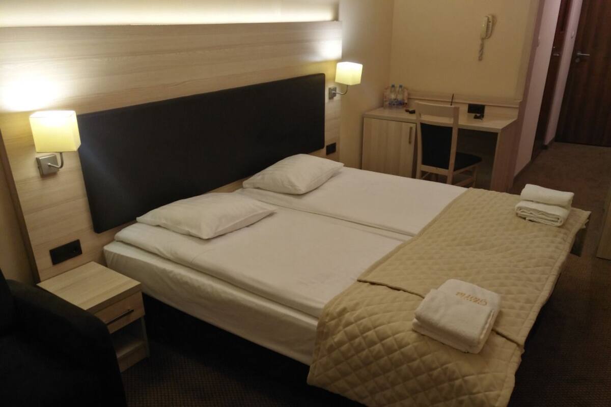 A hotel room with a bed, bedside tables, a desk, and a chair.