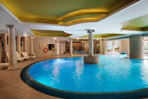 A large indoor swimming pool with clear blue water, surrounded by white columns and lounge chairs. - SPA Hotel Gloria (Przemysl)