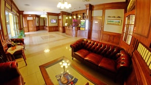 En lobby med lædersofa, træpaneler, reception og fjernsyn.