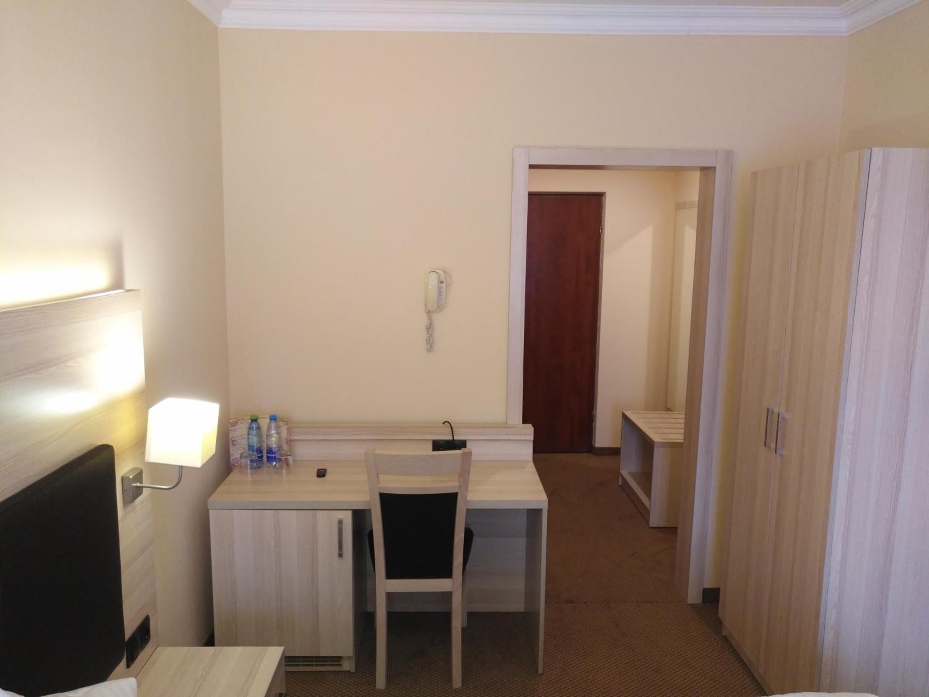 A hotel room with a bed, a desk, a chair, a telephone, and a wardrobe.