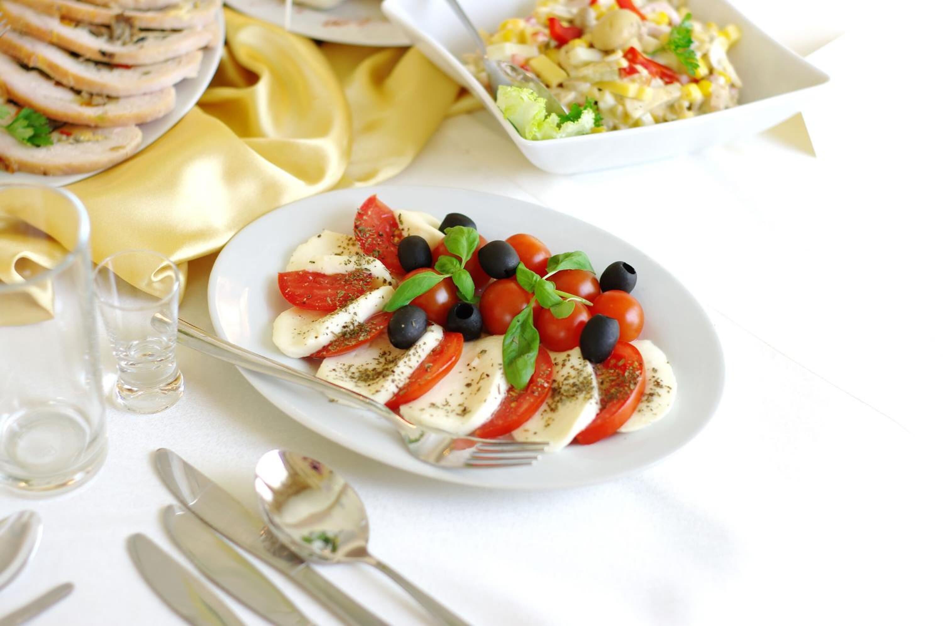 Une assiette de salade Caprese, composée de tomates, de mozzarella et de basilic, accompagnée d’une portion de viande tranchée et d’une salade servie dans un bol blanc.