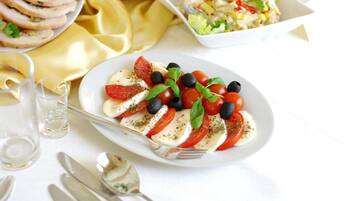 Une assiette de salade Caprese, composée de tomates, de mozzarella et de basilic, accompagnée d’une portion de viande tranchée et d’une salade servie dans un bol blanc.