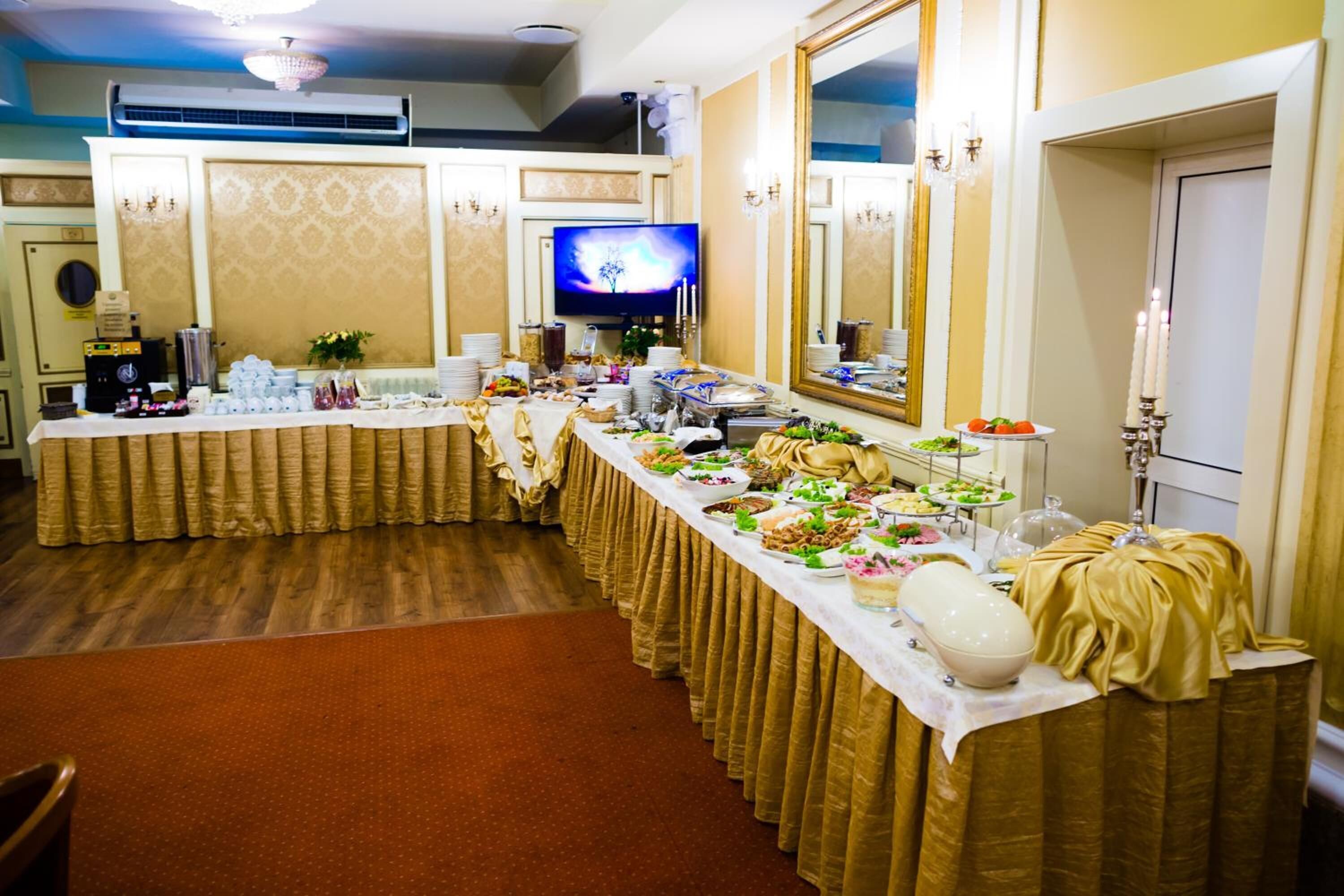 A buffet setup with a variety of dishes, a television, and a mirror in a room with patterned wallpaper and a chandelier.