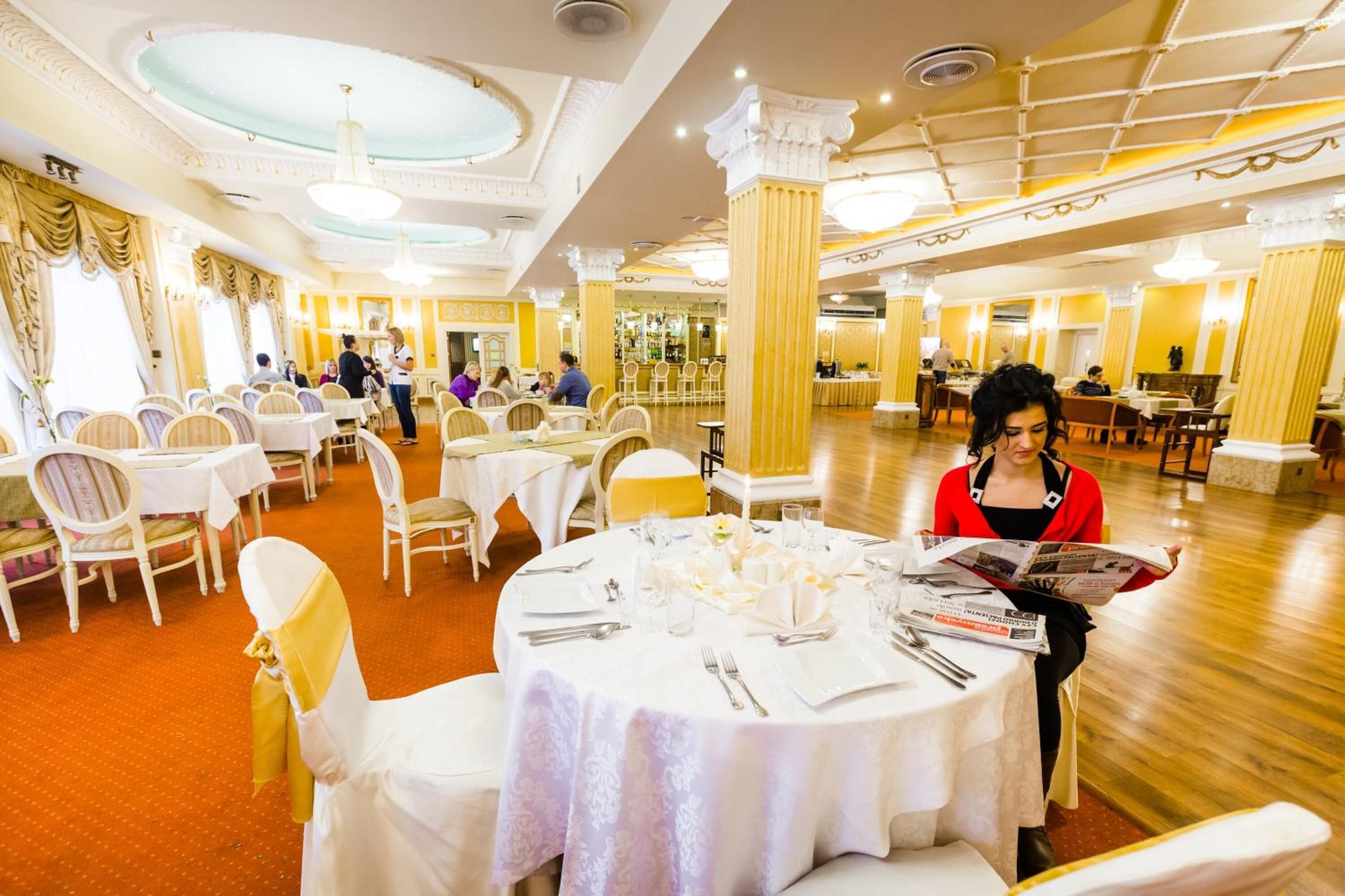 Un comedor de hotel amplio con mesas redondas, sillas blancas y una paleta de colores cálidos.