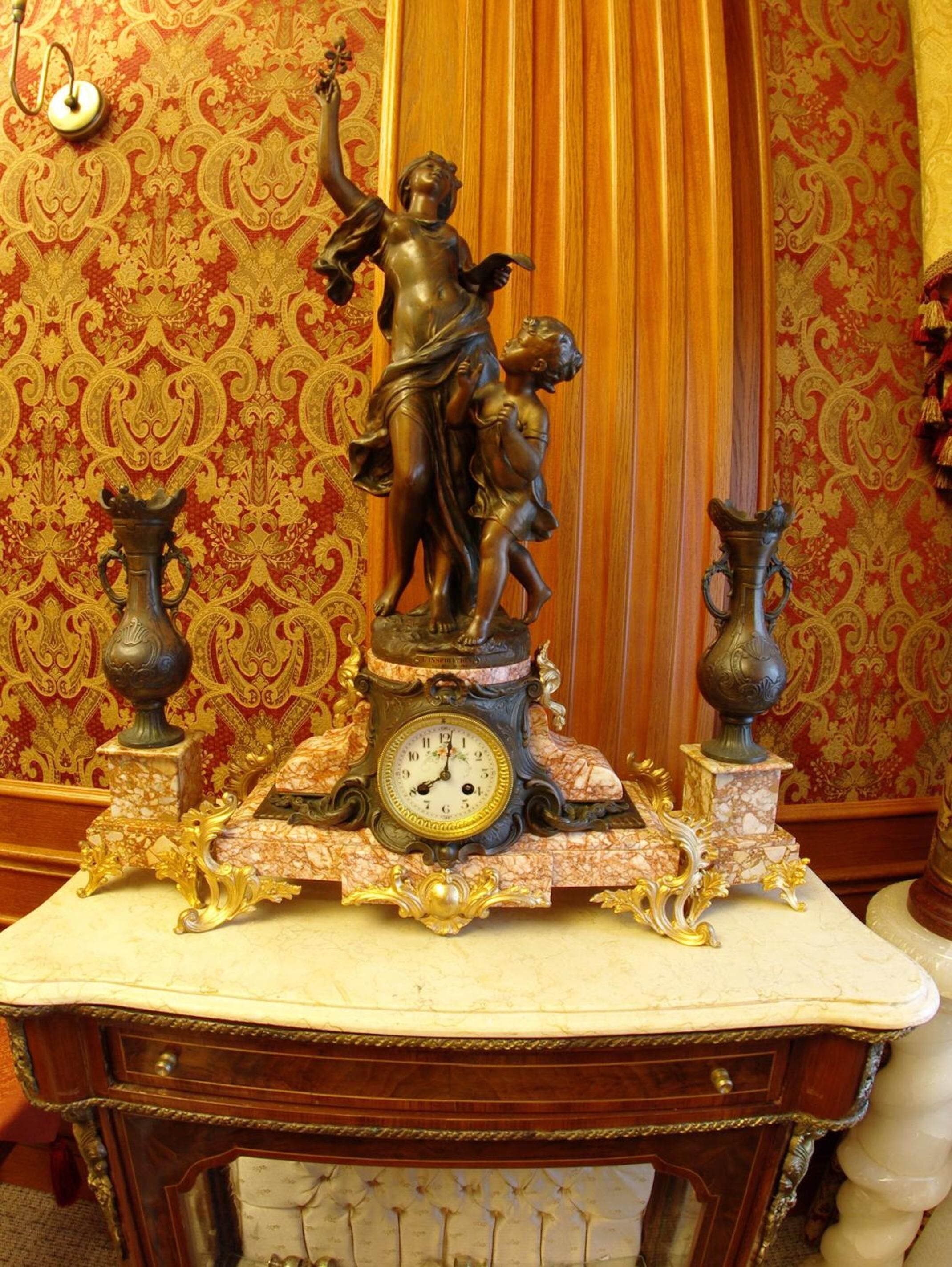 A clock with a statue of a woman and child on a marble table.