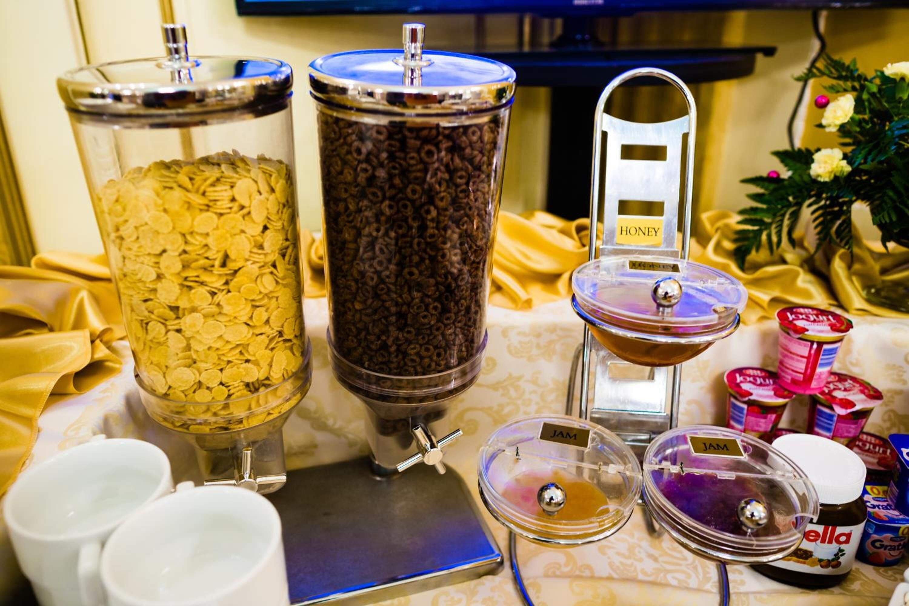 Disposición de buffet con opciones de cereales y café, incluyendo frascos etiquetados 'Honey' y 'Jam'.