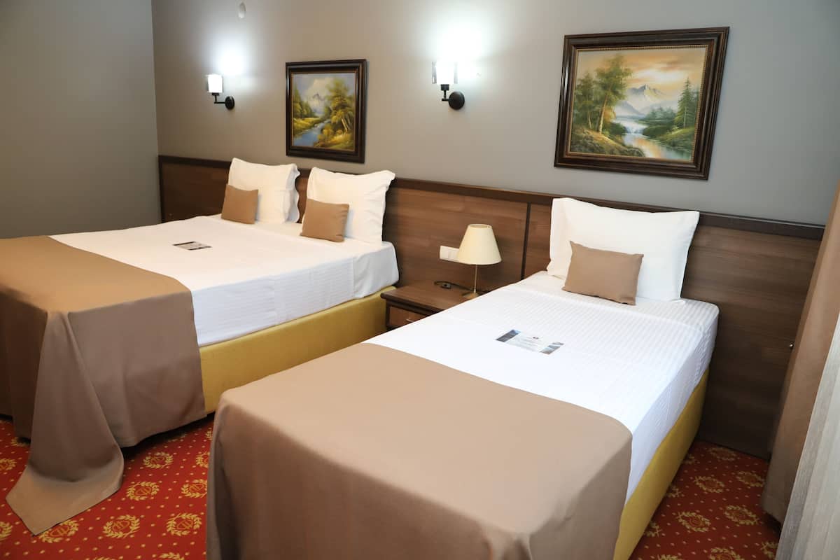 A hotel room with two single beds, a nightstand, a lamp, and two wall-mounted paintings.