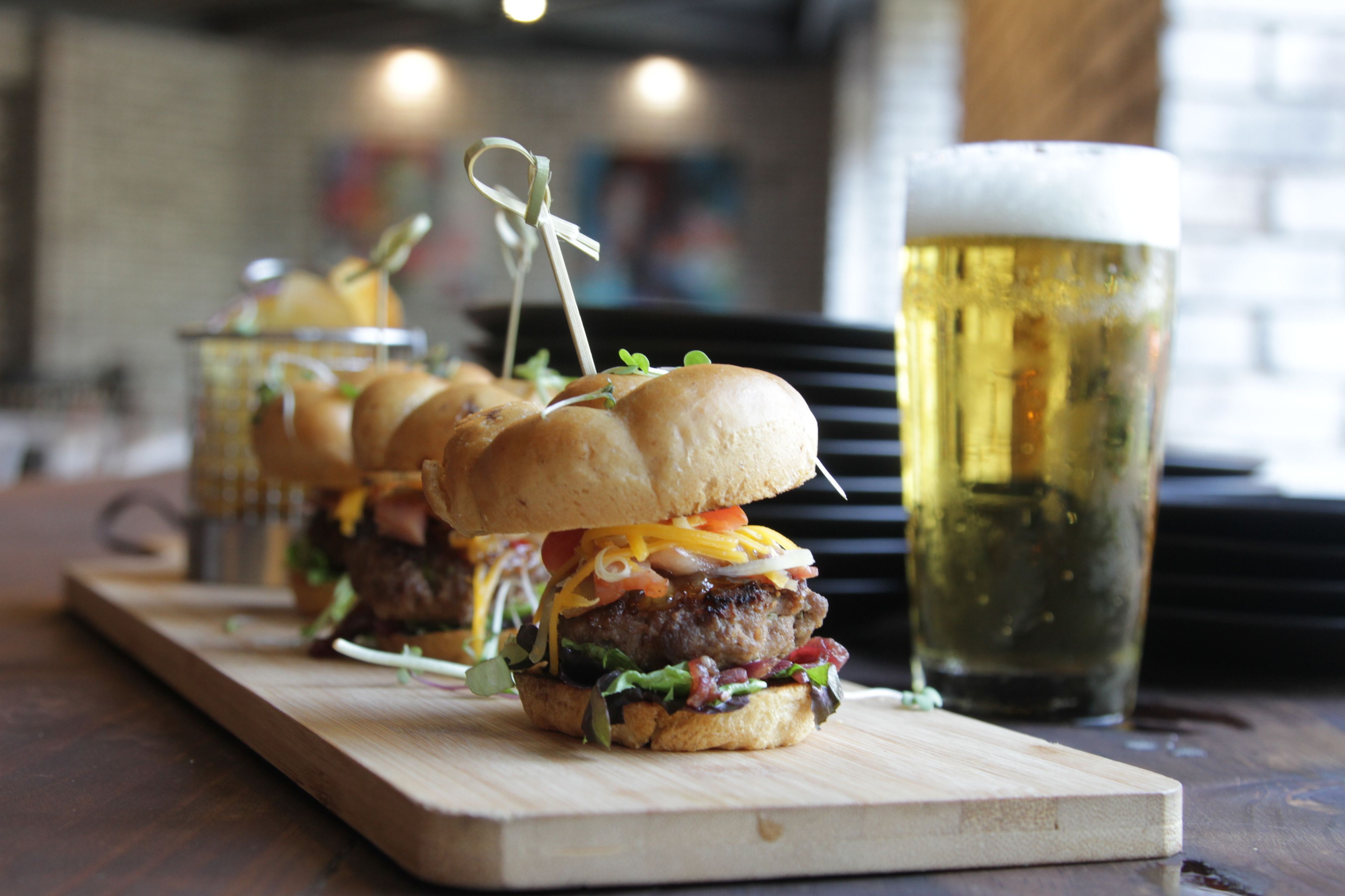 Una tabla de madera con tres hamburguesas y una jarra de cerveza.