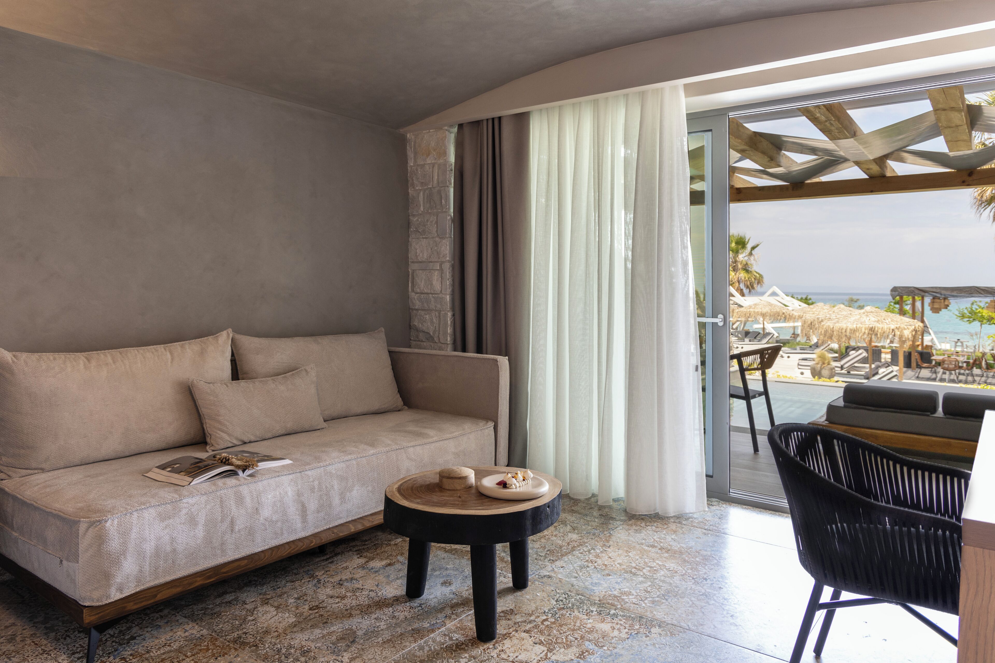 A modern room with a sofa, a small round table, and a view of the beach through a glass door.