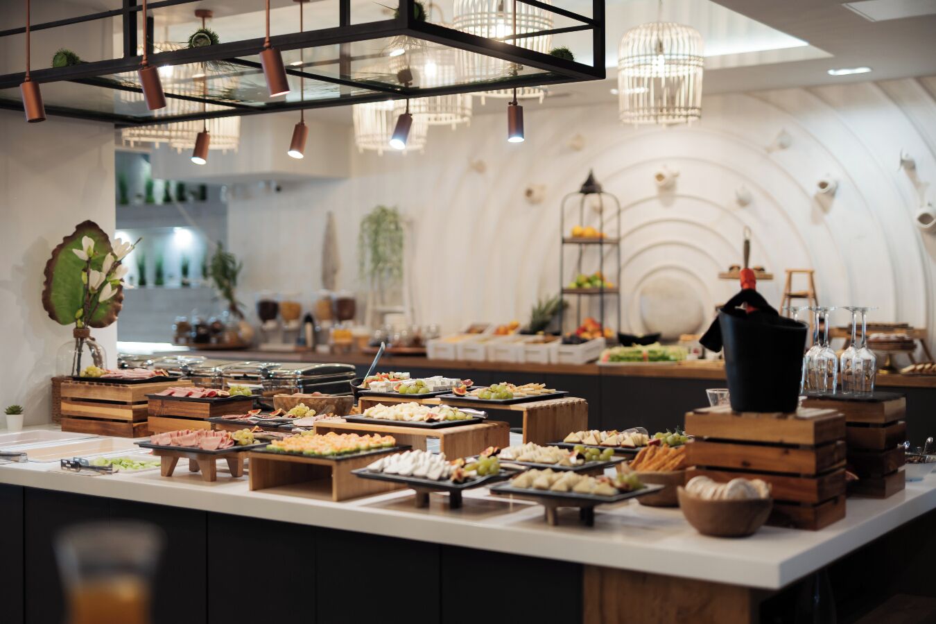 A buffet setup with various food items and drinks, wooden crates, and hanging lights.