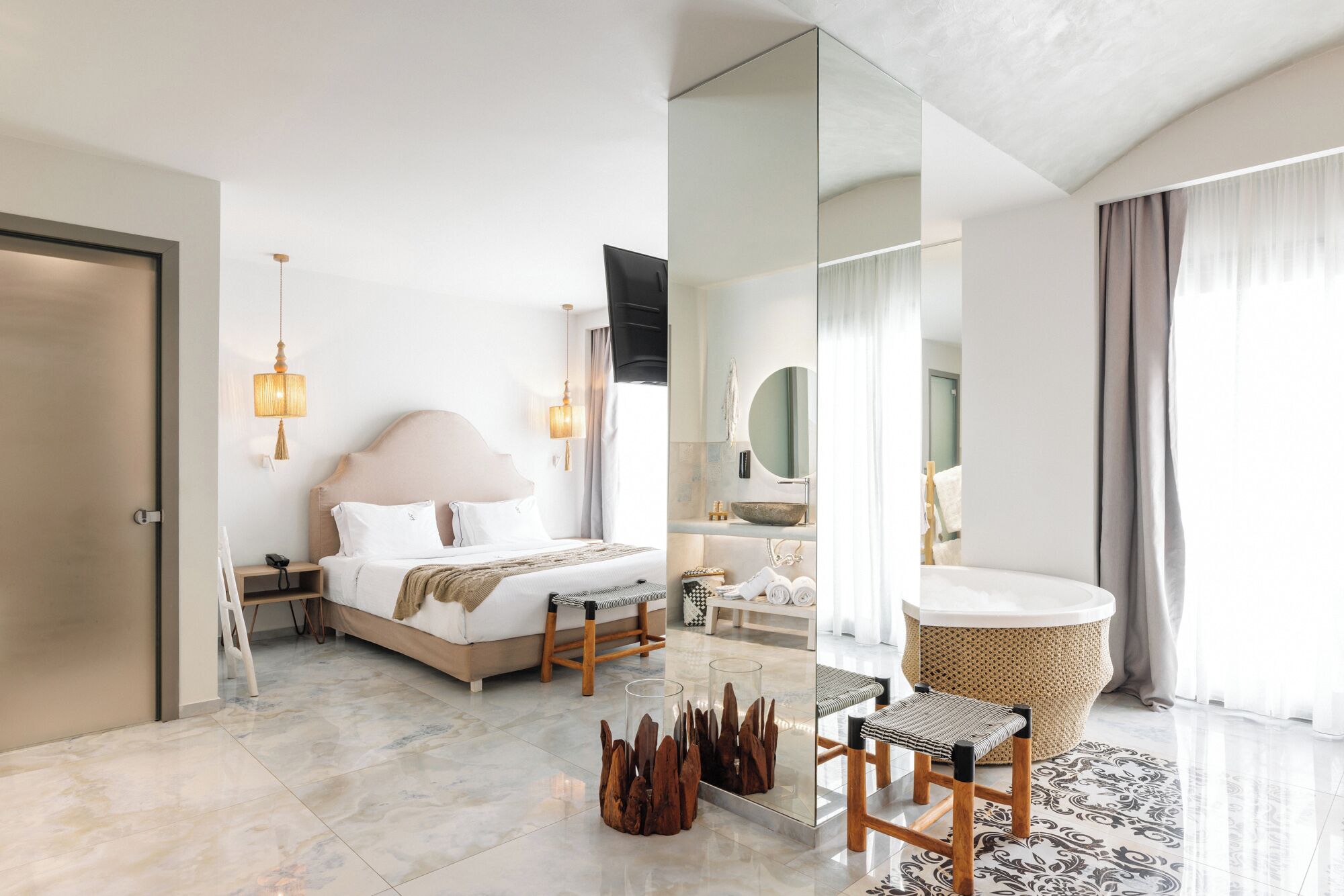 A modern hotel room with a large bed, bedside lamps, a vanity with a mirror, a round wooden stool, and a patterned rug.