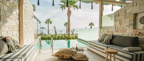 A modern lounge area with a pool view, stone walls, and a wooden ceiling.