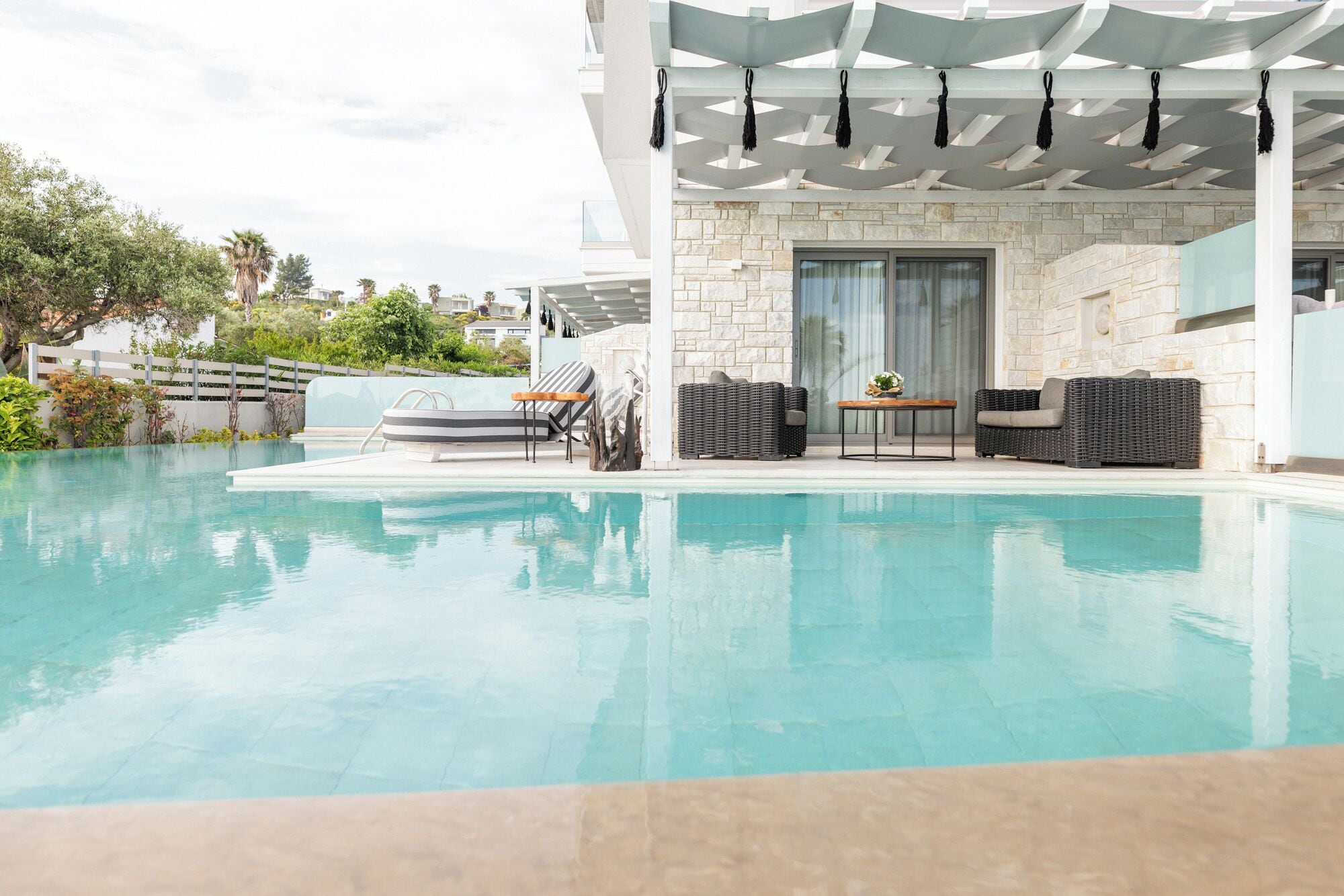 A modern outdoor pool area with a stone wall, lounge chairs, and a covered seating area.