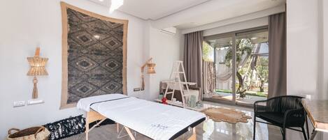 Una habitación moderna con cama, una silla, una mesita y un amplio ventanal con vistas al exterior.