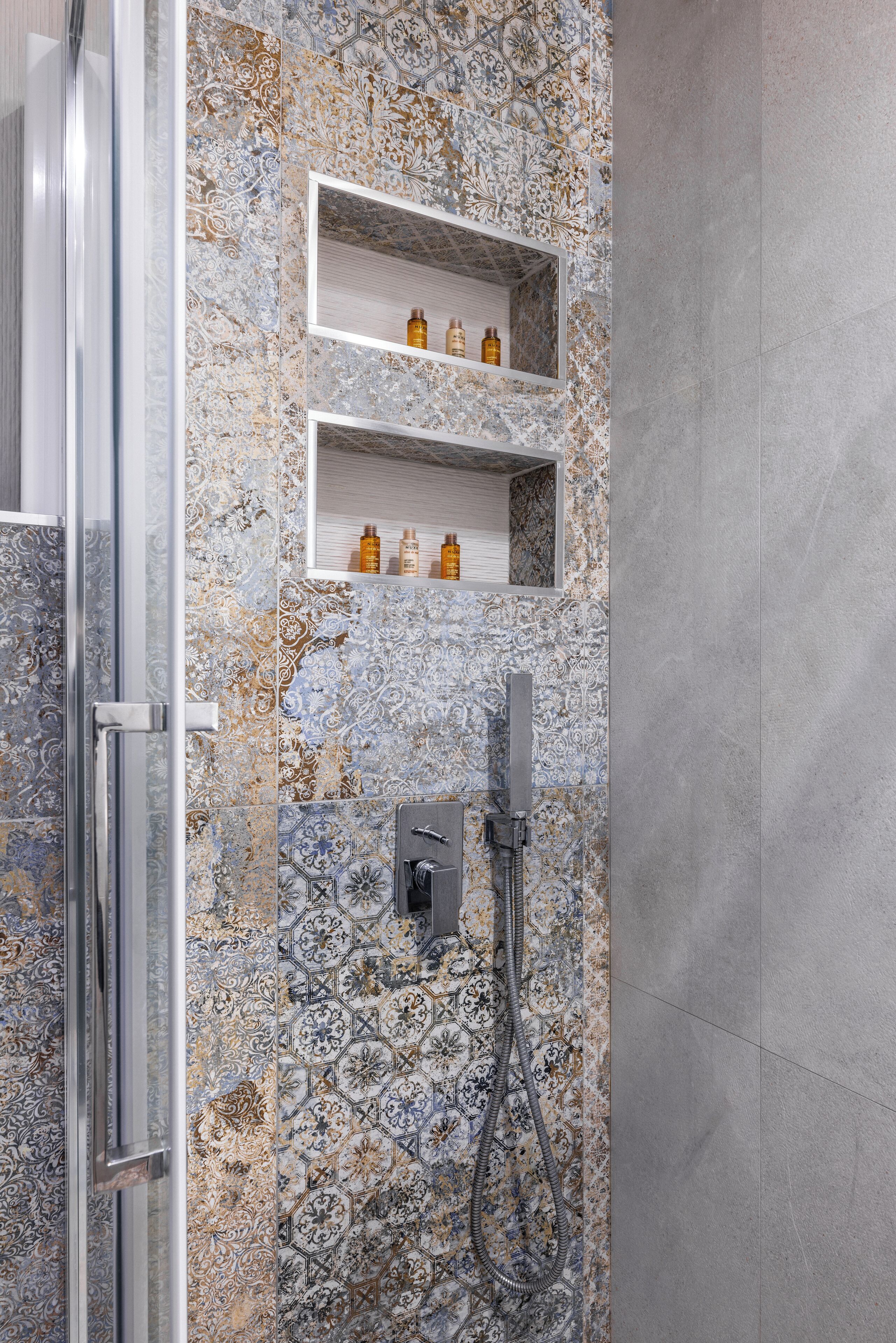 Un baño con zona de ducha, puerta de cristal y paredes de azulejos con diseños decorativos.