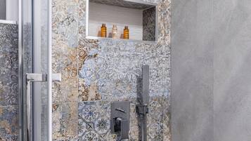 Un baño con zona de ducha, puerta de cristal y paredes de azulejos con diseños decorativos.