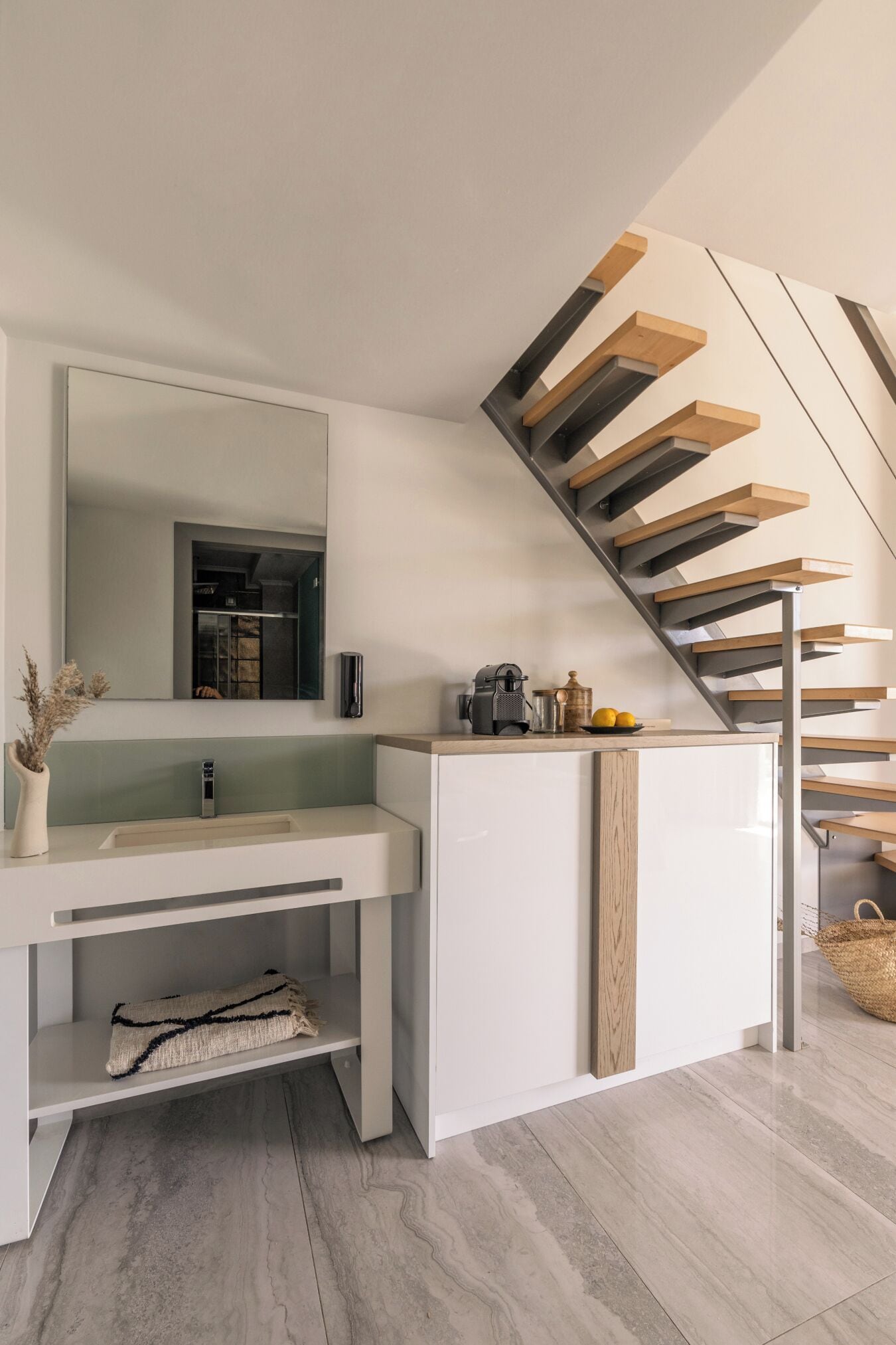 A modern bathroom with a white vanity, a large mirror, and a wooden staircase.