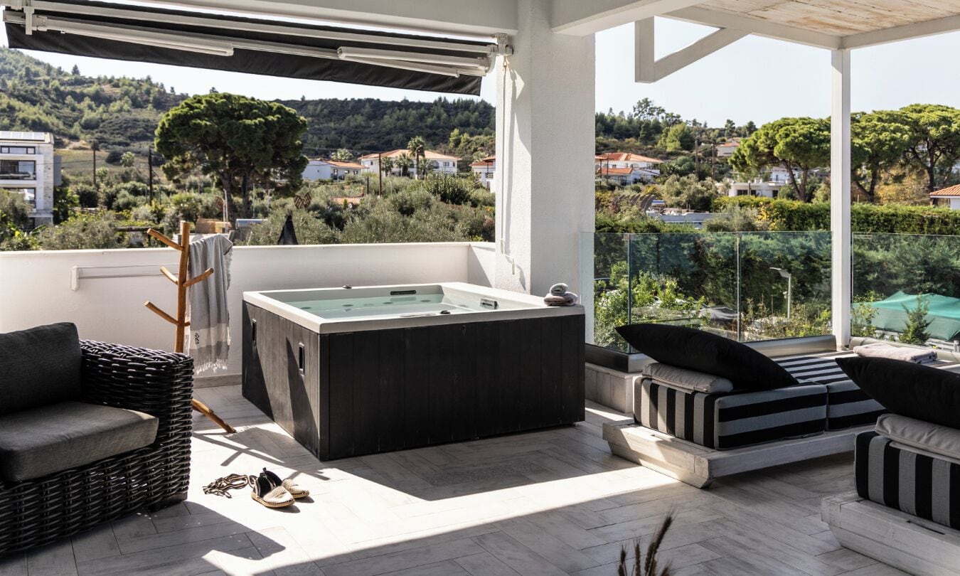 A balcony with a hot tub, wicker furniture, and a view of a hillside with houses.
