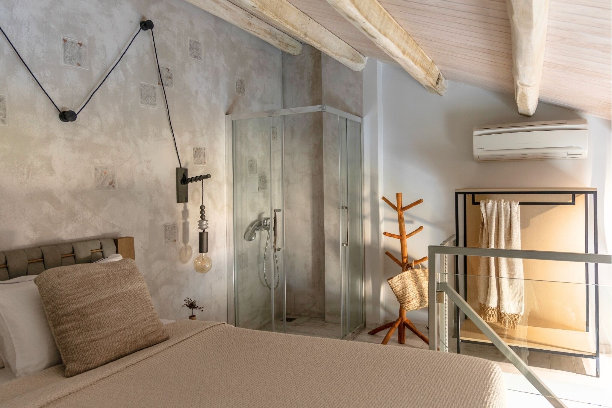A bedroom with a bed, a glass-enclosed shower, a wooden chair, and a staircase.