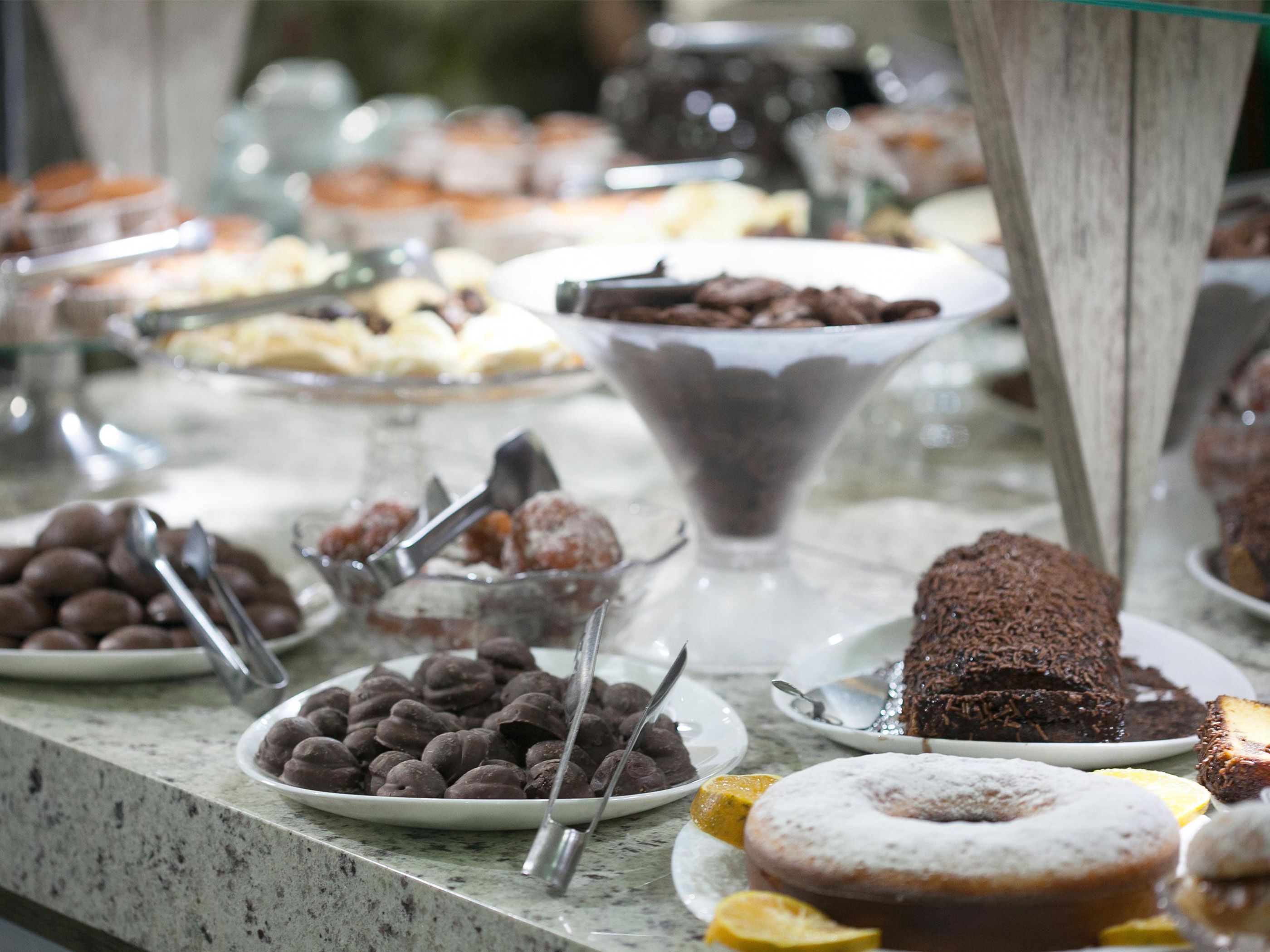 Uma mesa de buffet com diversos doces, incluindo itens cobertos com chocolate, um bolo e um donut.