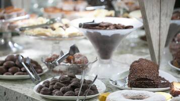 Uma mesa de buffet com diversos doces, incluindo itens cobertos com chocolate, um bolo e um donut.