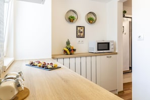Une cuisine moderne équipée d’un four à micro-ondes, d’un panier de fruits et d’une variété de pâtisseries disposées sur le comptoir.