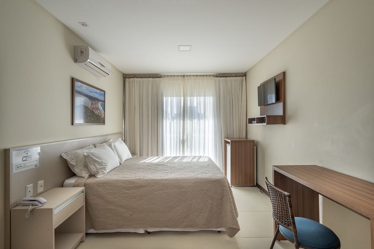 A hotel room with a bed, a desk, a chair, a TV, and a window with curtains.