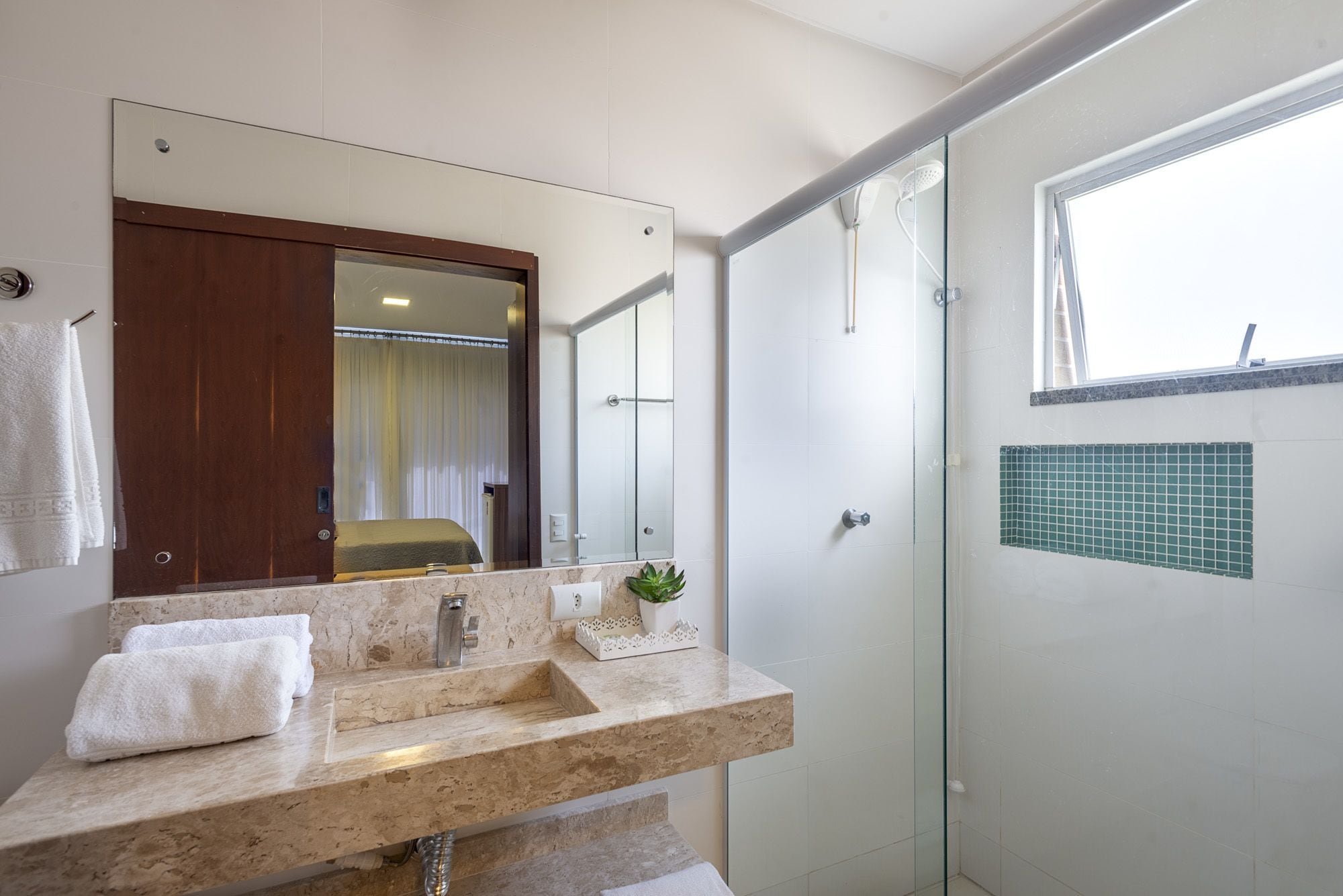 A modern bathroom with a marble sink, a large mirror, a glass shower enclosure, and a view of the outside.