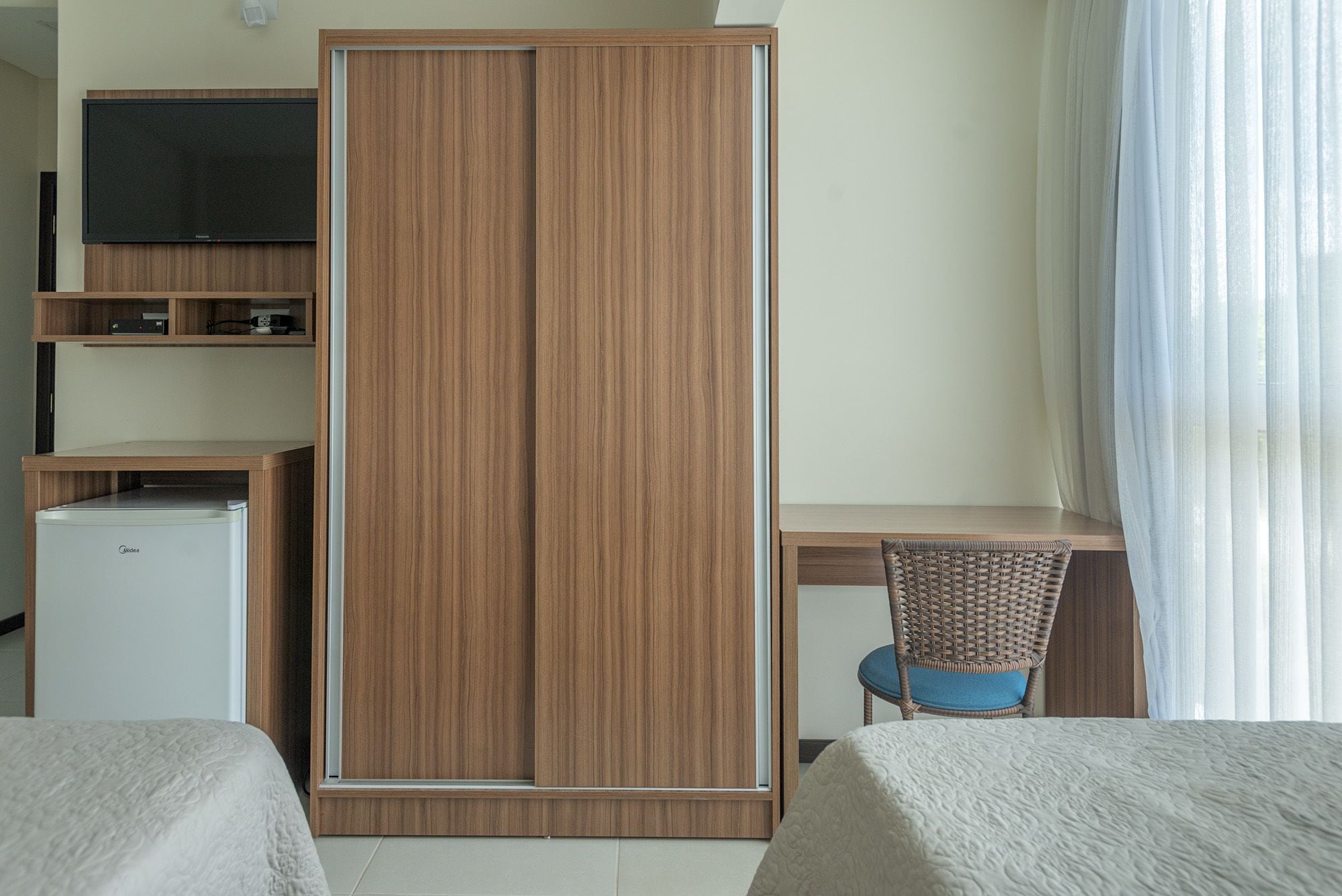 A hotel room with a wardrobe, a television, a desk, a chair, and a bed.