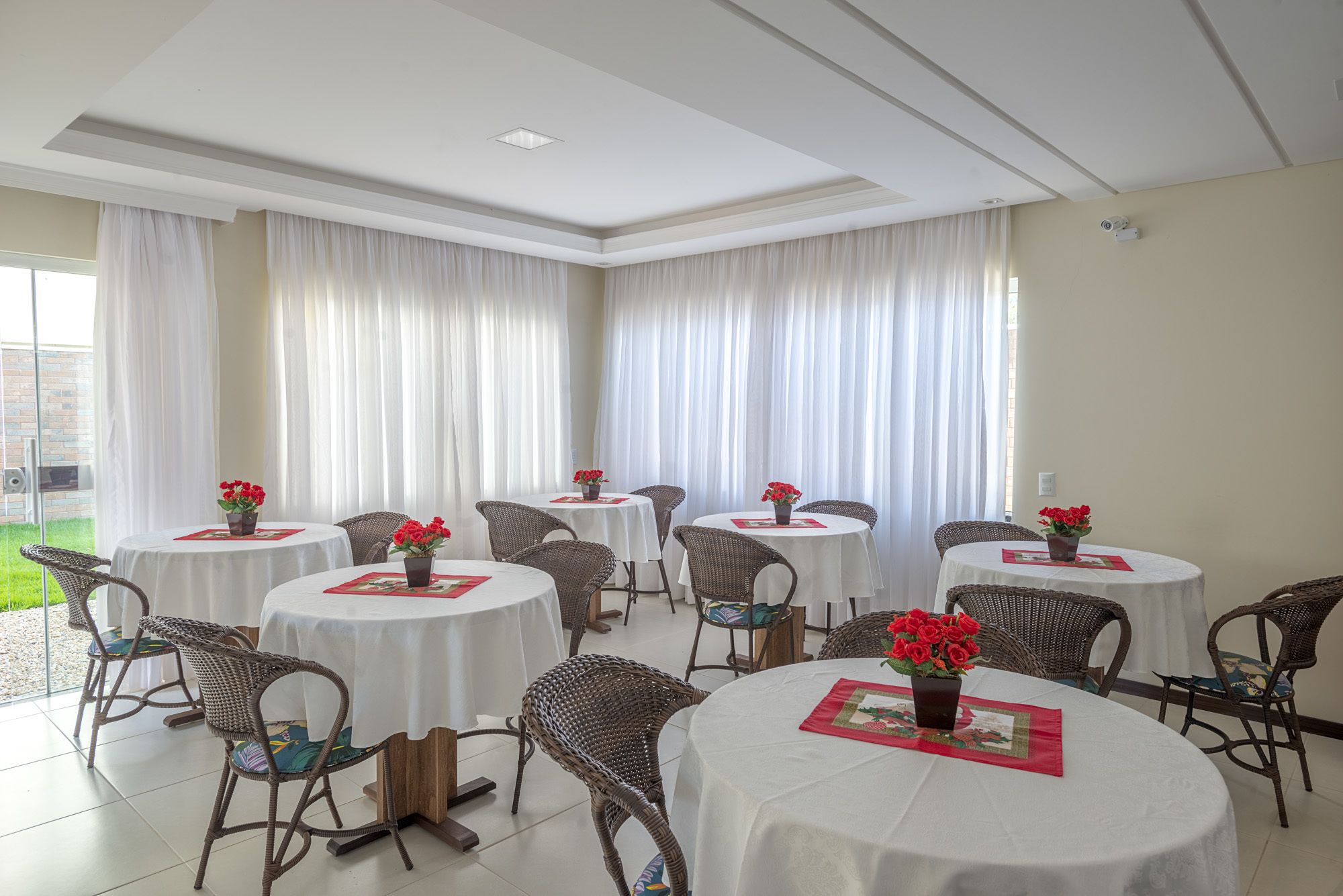 A dining area with round tables, wicker chairs, and red flowers on placemats.