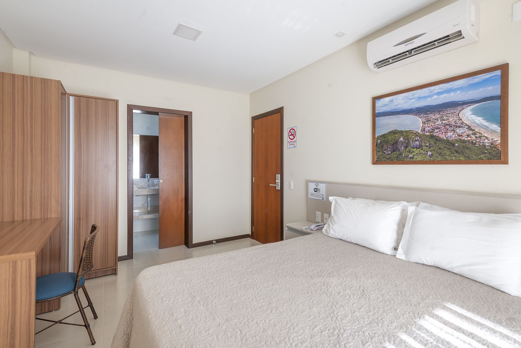 Habitación de hotel con cama, escritorio, silla, baño y un cuadro de un paisaje costero.