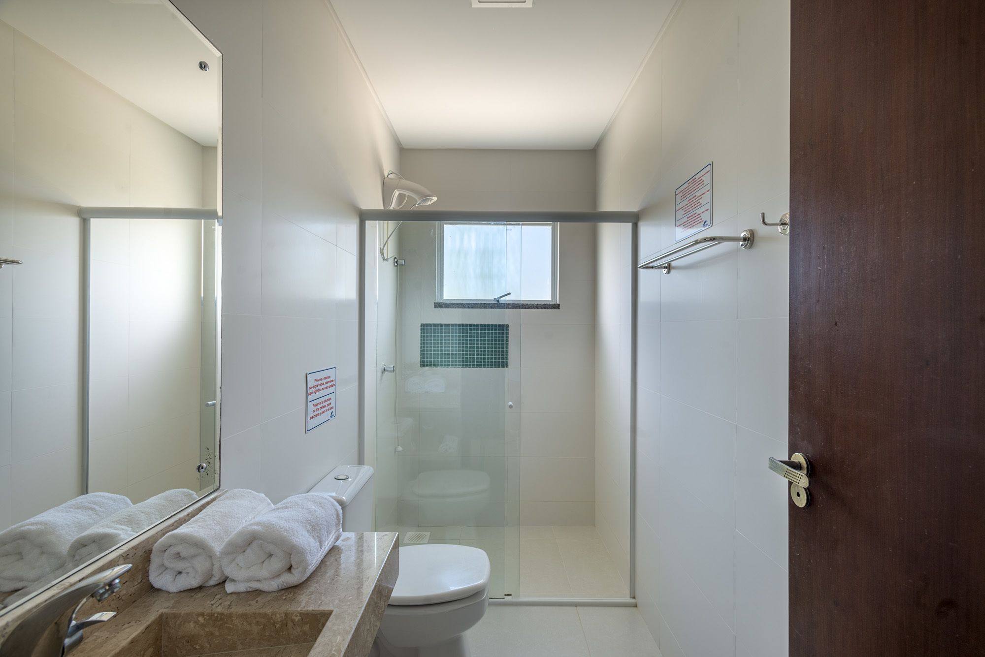 Une salle de bain moderne avec une douche à parois de verre, des toilettes et un lavabo doté d’un plan de travail en marbre. Des serviettes sont soigneusement pliées sur le lavabo et un panneau est accroché au mur.