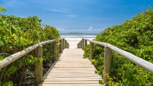 A wooden pathway leading to a beach with lush greenery on both sides.