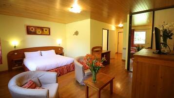 A hotel room with a wooden ceiling, two beds, a sitting area with a chair and table, and a small desk with a vase of flowers.