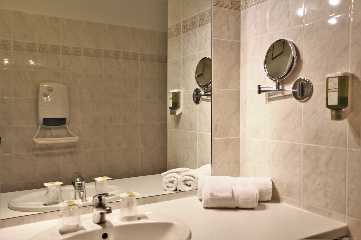 A modern bathroom with a sink, mirror, towel, and soap dispenser.