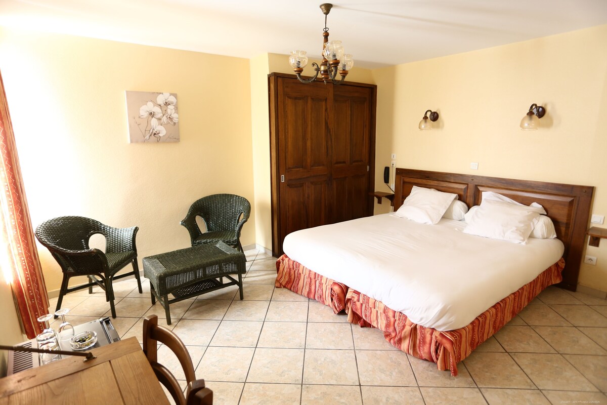 A hotel room with a large bed, two wicker chairs, a wooden door, and a chandelier.