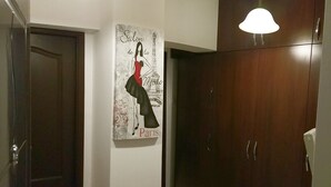 A hallway with a dark wooden wardrobe, a door, and a wall-mounted poster of a woman in a dress with the words "Salon de la Mode Paris". - Sudului 810 by MRG Apartments (Bucharest)