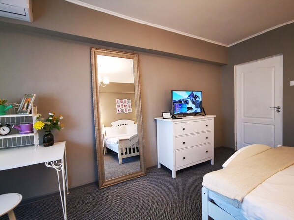 Une chambre à coucher comprenant un lit, une commode, un bureau, un miroir et un téléviseur.