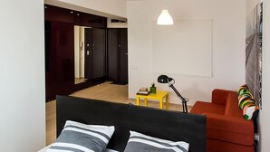 Un dormitorio moderno con una cama, una silla roja, una mesita de noche con una lámpara y un espejo.