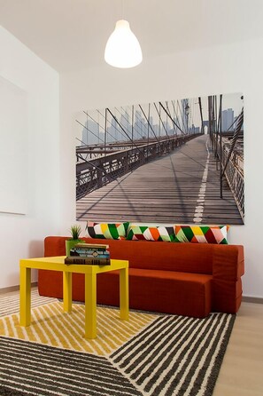 A modern living room with a red sofa, a yellow coffee table, and a cityscape painting on the wall. - Studio R by MRG Apartments (Bucharest)