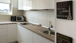 Una cocina moderna con armarios blancos, un lavamanos de acero inoxidable y un microondas. Hay dos letreros en la pared, uno con texto relacionado con París y otro con texto relacionado con Londres.
